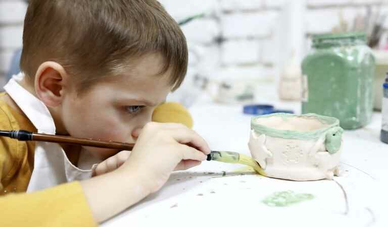 boy painting with acrylic on mug
